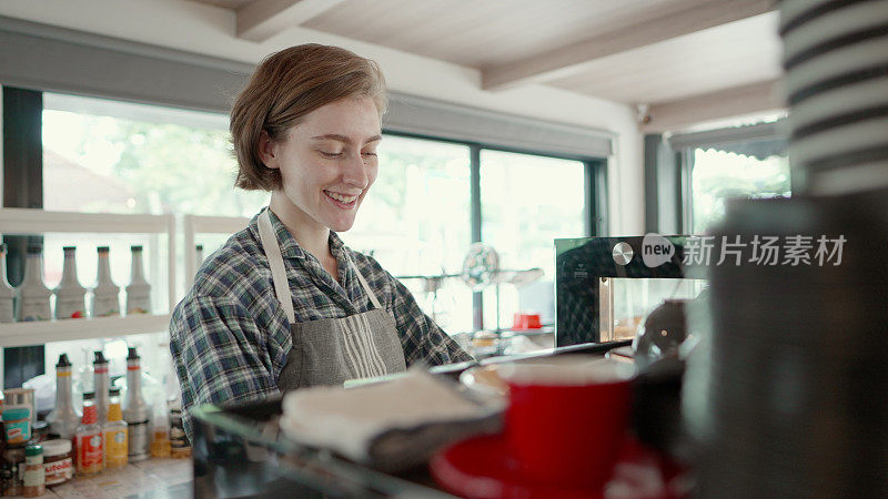 Young barista making coffee for customers at the Café. Entrepreneur or employee standing behind the counter ready to serve customers or barista take the order in cafe. Young females business owner or manager working in coffee shop.